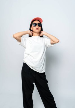 Beyaz gömlekli, şapkalı ve gözlüklü beyaz arka planda poz veren genç bir kadın.