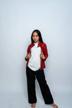 Beyaz gömlekli ve deri ceketli genç bir kadın beyaz arka planda ciddi bir poz veriyor.