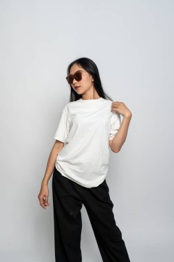 Beyaz gömlekli ve gözlüklü genç bir kadın beyaz arka planda havalı bir poz veriyor.