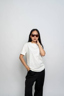 Beyaz gömlekli ve gözlüklü genç bir kadın beyaz arka planda havalı bir poz veriyor.