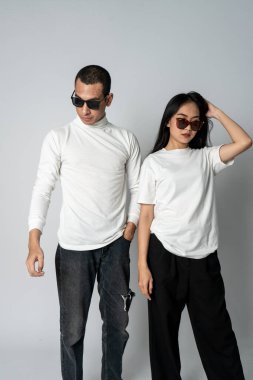 Beyaz gömlekli ve gözlüklü havalı poz veren bir çift. Beyaz bir arka plan.