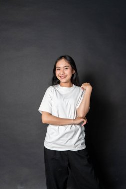 Beyaz gömlekli Asyalı bir kadın siyah arka planda mutlu poz veriyor.