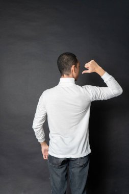 Kısa saçlı, beyaz, balıkçı yaka bir gömlek giyen genç bir adamın arka tarafı. Siyah arka planlı, sırtına doğru poz veriyor.