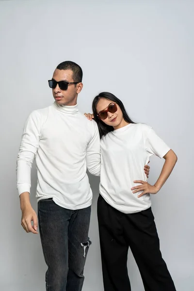 A couple wearing white blank shirt and a glasses posing while the woman leaning her head to the man on a white background