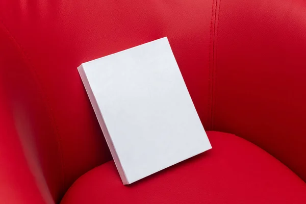 Image of a blank white hardcover book on the top of a red sofa for mockup