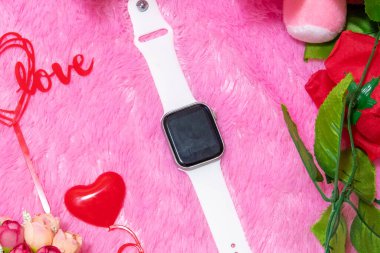 Sevgililer günü temalı dekorasyonlarla çevrili boş ekran ve arka planda tüylü pembe bir halı ile akıllı bir saat.