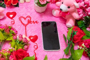 Oyuncak bebekler ve çiçeklerle çevrili akıllı telefon ekranının maketi ve arka plan olarak da pembe tüylü bir halı.
