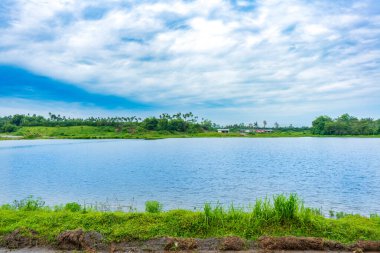 Bir sürü ağacın olduğu bir manzara, ıssız bir pavyon, bir göl, ve mavi renkli gökyüzü, görünür bir bulut, renkli bir manzara.