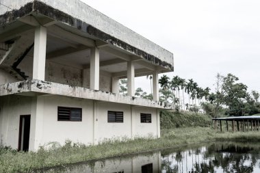 Terk edilmiş, iki katlı, bitmemiş bir binanın yan görüntüsü. Korku titreşimli bir parkın yanındaki gölete inşa edilmiş.