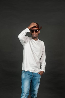 Beyaz gömlekli bir adam siyah arka planda dikilirken poz veriyor.