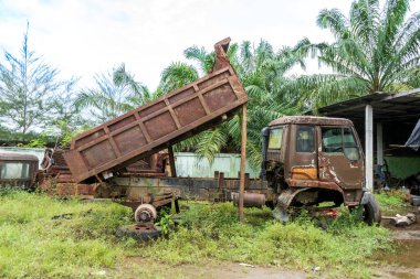 Kırık kahverengi bir kamyonun yan görüntüsü, konteynırı yarı kaldırılmış, öğle vakti alınmış.