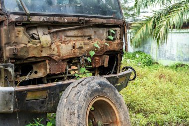 Kırık bir kamyonun ön tarafında, büyük siyah lastikleri olan, öğle vakti araca doğru eğilen,