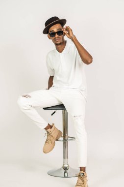 Polo tişörtlü Afrikalı bir adamın beyaz arka planı olan bir sandalyenin üstünde otururken ki görüntüsü.