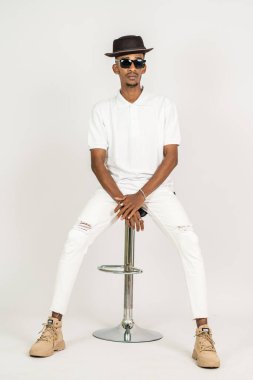 Polo tişörtlü Afrikalı bir adam beyaz arka plan görüntüsü olan bir sandalyenin üstünde oturuyor.