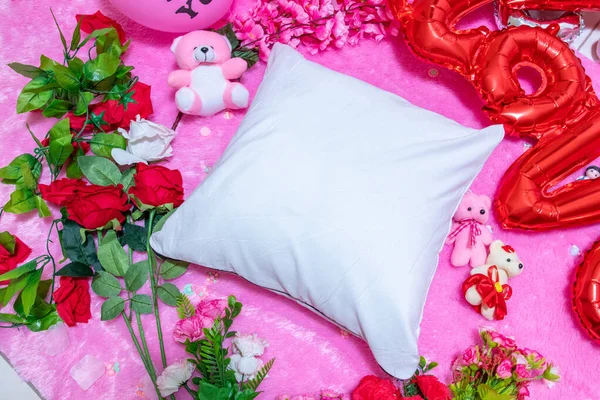 White blank pillow above a a fluffy pink carpet surrounded by valentine themed decorations