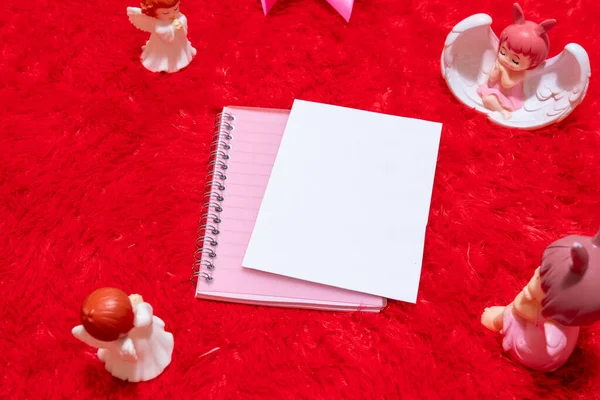 White blank notebook paper on the top of a notebook surrounded by valentine themed decorations, and a red fluffy carpet as the background