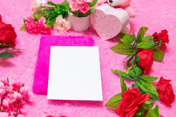 Sevgililer günü temalı dekorasyonlarla çevrili pembe kaplı bir defterin üzerinde beyaz, boş bir defter ve arka plan olarak da pembe, tüylü bir halı.