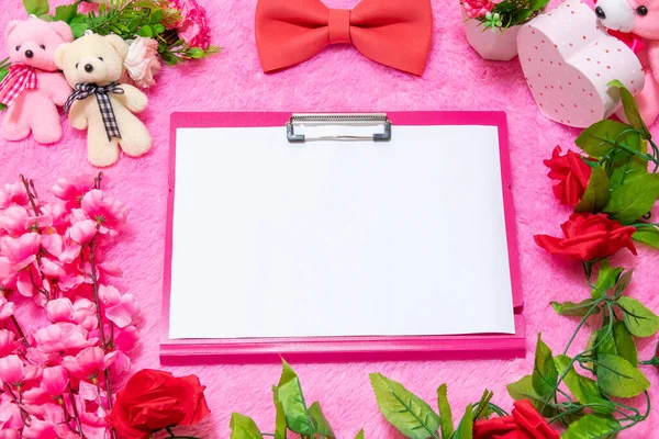Sevgililer günü temalı dekorasyonlarla çevrili pembe bir panonun üstünde beyaz, boş bir A4 kâğıdı ve arka plan olarak da pembe, tüylü bir halı.