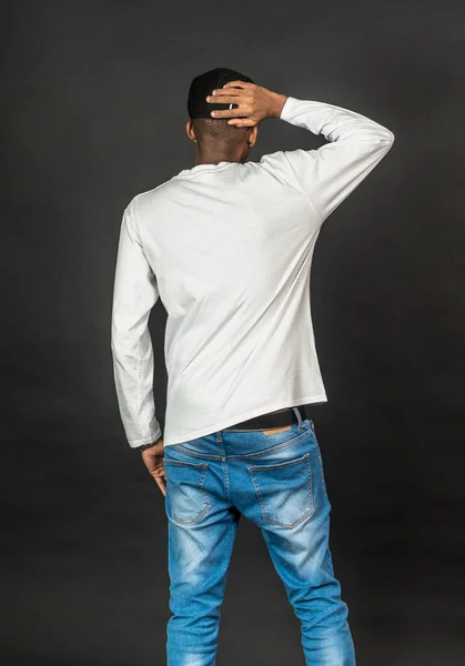 Back side of an african man with white shirt and a hat doing a pose, on the black background