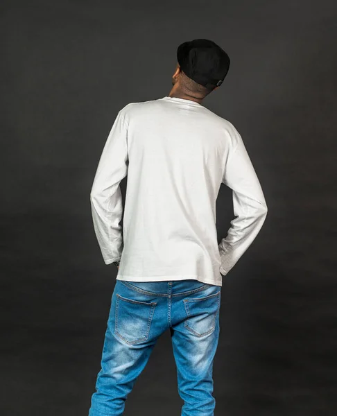 Back side of an african man with white shirt and a hat doing a pose, on the black background