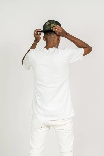 Back side of an african man with white shirt doing a pose while touching his hat on the white background