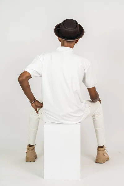Back side of an african man wearing a polo shirt sitting on the top of a white box with white background mockup image