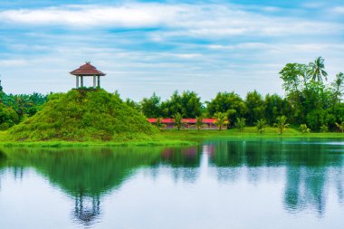 Ağaçlarla dolu bir manzara, ıssız bir pavyon, bir göl, ve mavi bir gökyüzü, görünür bulutlu, renkli manzaralı.