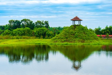 Ağaçlarla dolu bir manzara, ıssız bir pavyon, bir göl, ve mavi bir gökyüzü, görünür bulutlu, renkli manzaralı.