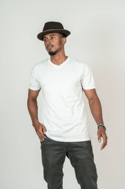 Beyaz v yakalı beyaz tişörtlü Afrikalı bir adam beyaz arka planda, yana bakarken poz veriyor.