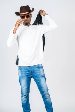 Beyaz, boş gömlekli bir adam beyaz arka planda deri ceketini tutarken poz veriyor.