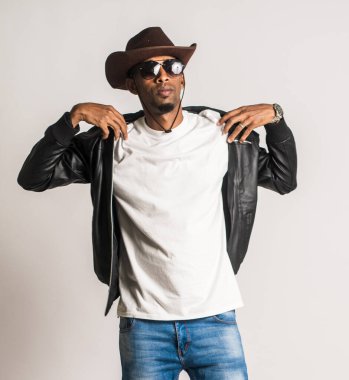 Beyaz gömlekli bir adam beyaz arka planda deri ceketine dokunurken poz veriyor.
