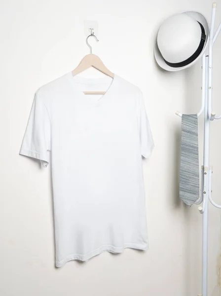 A v neck shirt hanged on to a hook at the wall, with a hat and tie hanged beside it, minimalist decorations