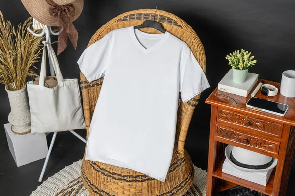 A v neck shirt hanged on to a chair with, with a hat and a tote bag hanged beside it, minimalist decorations