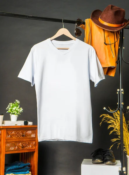 A v neck shirt hanged on the hook at the wall , with a leather jacked hanged beside it, minimalist decoration