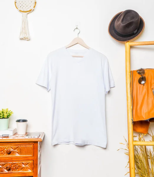 A v neck shirt hanged on the hook at the wall, with a leather jacked hanged beside it, minimalist decoration