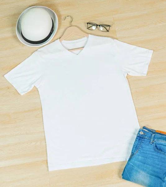 A v neck shirt laid out on the top of the wooden tiling, with a round hat and a jeans near it, minimalist decoration