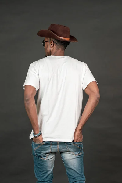 Back side african man wearing a white blank shirt doing a pose, on the black background mockup image