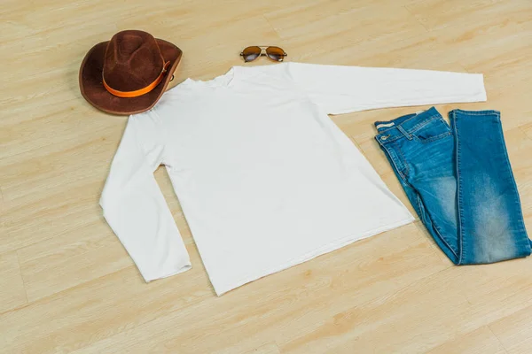 Tahta döşemelerin üstüne bir gömlek serilmiş, yanında şapka ve kot pantolon, minimalist dekorasyon.