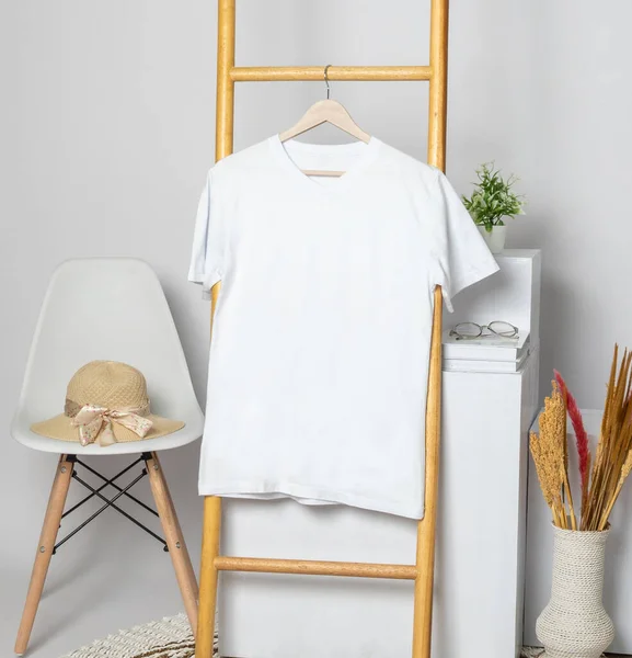 A v neck shirt hanged on to a wooden ladder with rustic leaves, minimalistic decorations
