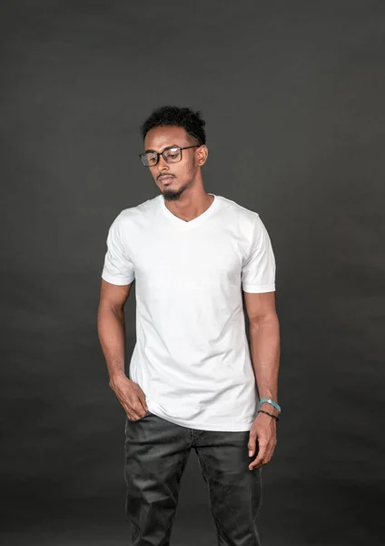 An african man with blank white v-neck shirt doing a pose while putting one of his hand on the pocket, on the black background