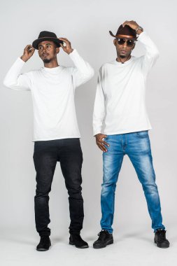 Beyaz, uzun kollu gömlekli, beyaz arka planda poz veren iki Afrikalı adam.