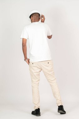 Beyaz, boş tişörtlü, gözlüklü, şapkalı, eli cebinde, beyaz arka planda poz veren bir gencin arkası.