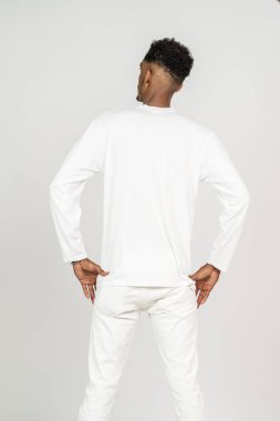 Beyaz, boş, uzun kollu gömlek giyen, elleri belinde, beyaz arka planda poz veren Afrikalı bir adamın arka yüzü.