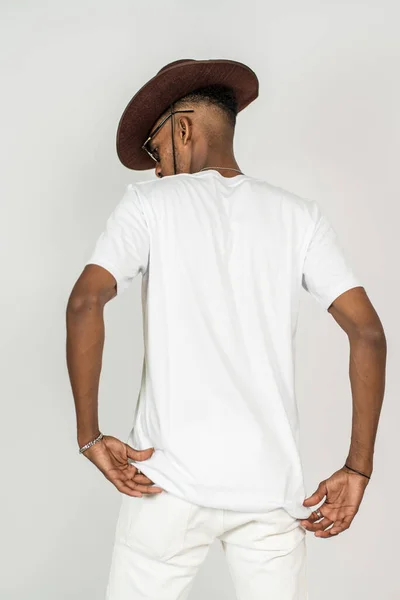 Back side of an african man wearing white blank shirt and a hat doing a simple pose, on the white background