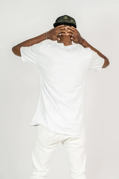 Back side of an african man wearing white blank shirt and a hat doing a simple pose by putting both of his hand on his back neck, on the white background