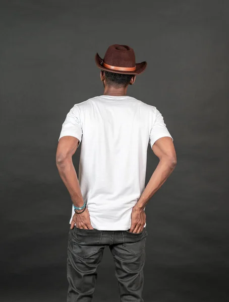 Back side image of an african man wearing white blank shirt with a hat, doing a simple pose, on the black background