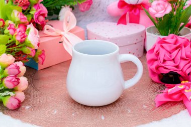 Sevgililer günü temalı dekorasyonlarla çevrili yuvarlak masa örtüsünün üzerinde beyaz, boş bir krema kupası.