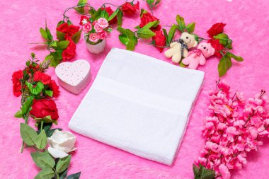 Pembe bir halının üzerinde beyaz boş havlu ve sevgililer günü temalı dekorasyonlarla çevrili.