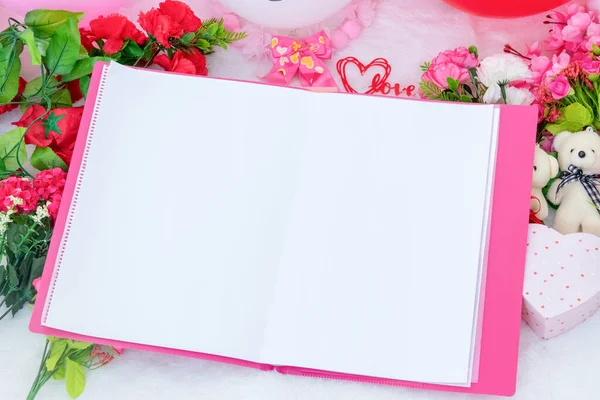 White blank A4 paper on the top of a pink file folder surrounded by valentine themed decorations, and a fluffy white carpet as the background