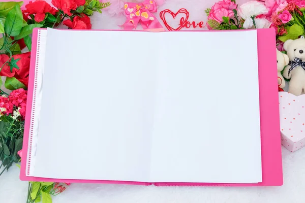 White blank A4 paper on the top of a pink file folder surrounded by valentine themed decorations, and a fluffy white carpet as the background